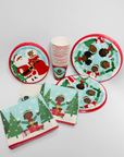 Christmas-themed paper plates, cups, and napkins with multicultural characters on a white background.