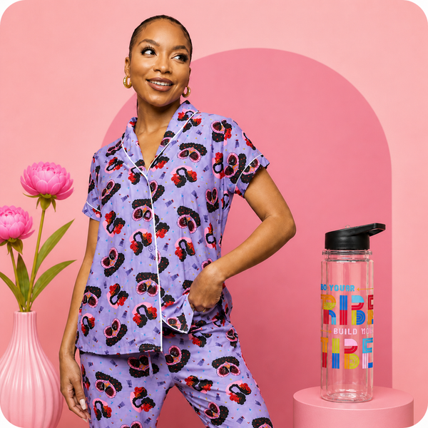 Woman wearing a purple pajama set with cherry pattern, standing next to a colorful water bottle on a pink background.
