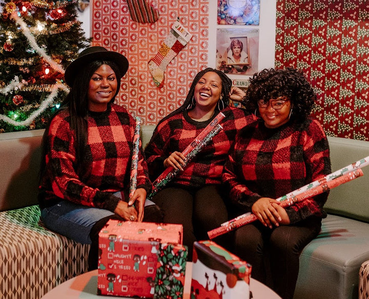 Madia, Jasmine, and Jae wearing red and black flannel shirts and holding black paper party wrapping paper. 