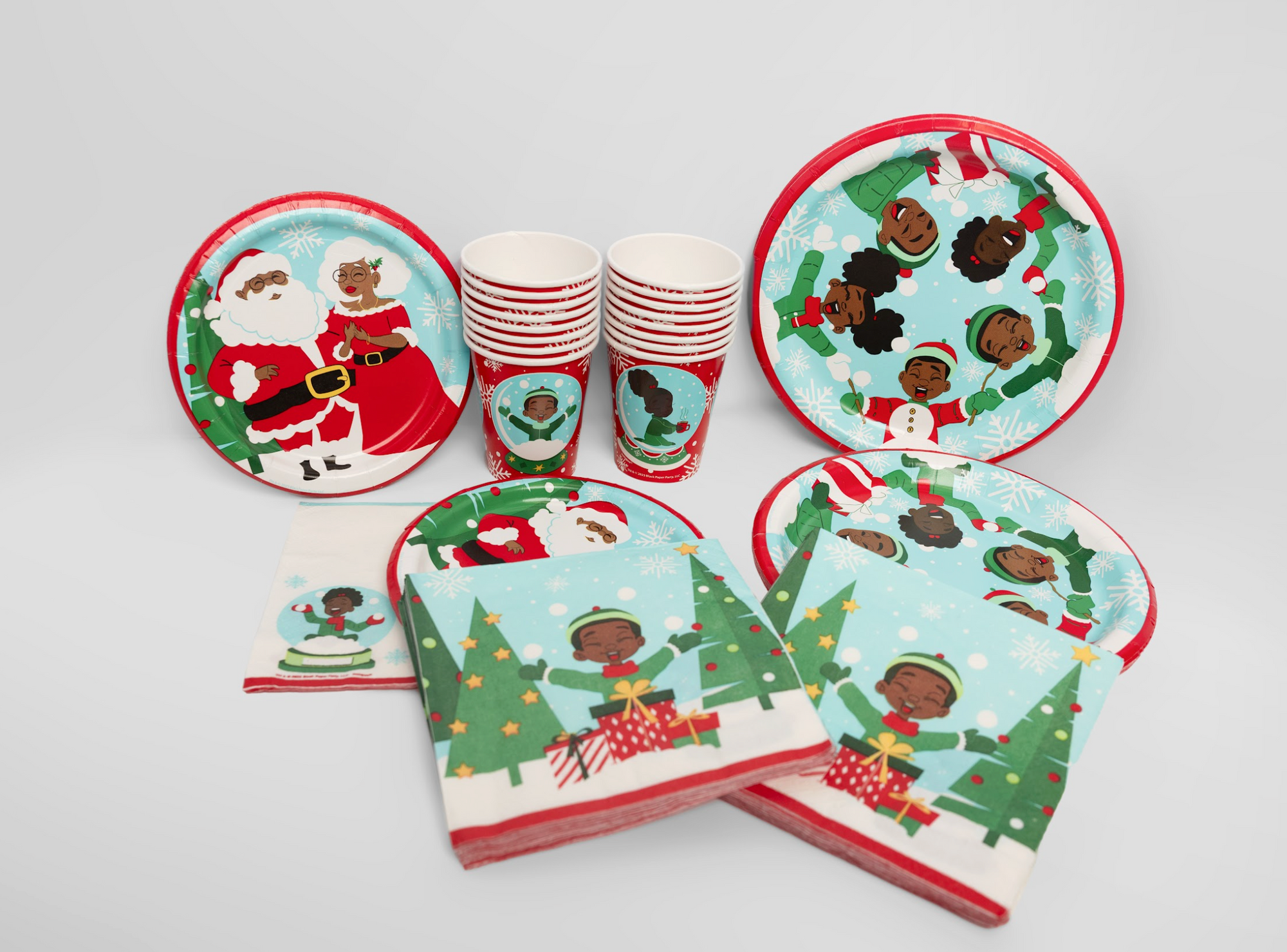 Christmas-themed paper plates and cups with multicultural characters on a white background