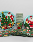 Christmas-themed paper plates, cups, and napkins on a light gray background