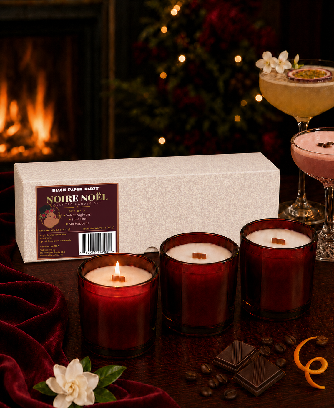 Three lit Noire Noel candles styled beside a fireplace with cocktails.