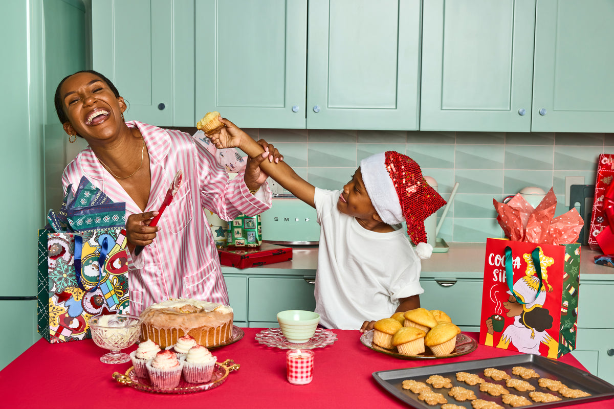 A Black mother and child laughing together while baking holiday treats in a festive kitchen